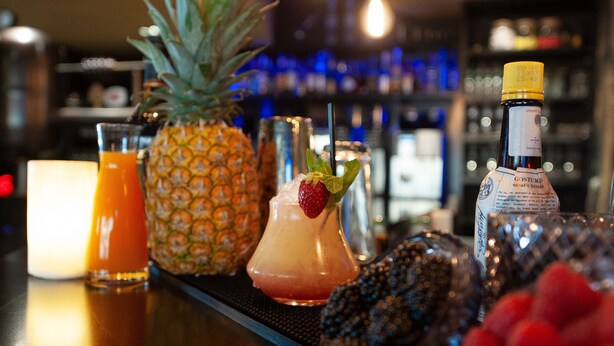 A bar area with a pineapple, a cocktail, a bottle of liquor, and a candle. - Hôtel Nota Bene (Montceau-les-Mines)