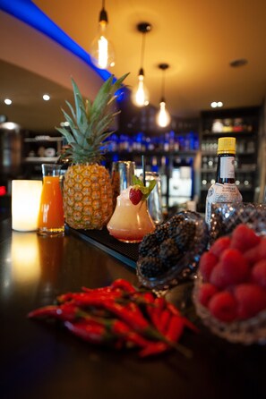 A bar area with a pineapple, a cocktail, a bottle of liquor, and a candle. - Hôtel Nota Bene (Montceau-les-Mines)