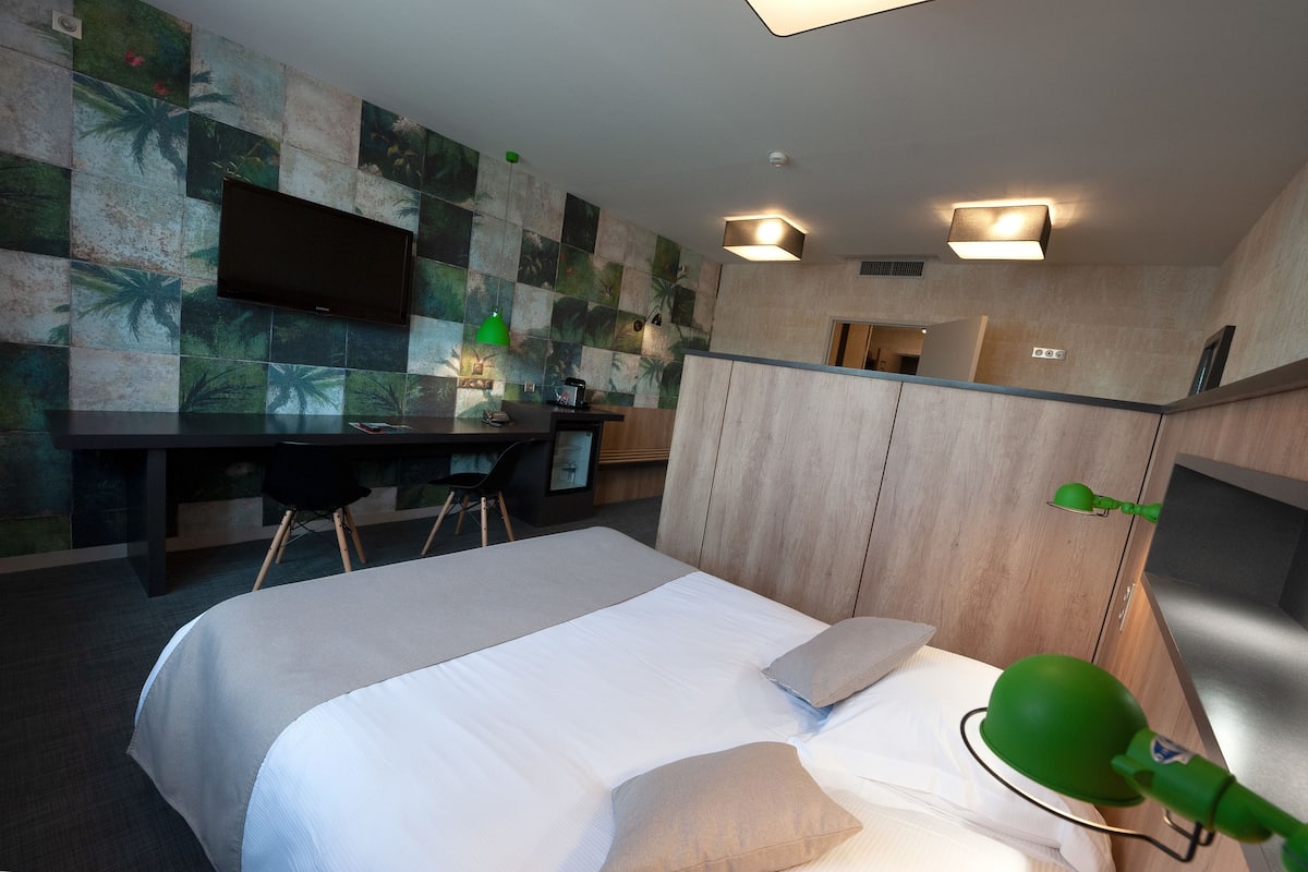 Ein Hotelzimmer mit Bett, Schreibtisch, Stuhl, Fernseher und einer grünen Lampe.