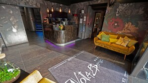 A hotel lobby with a reception desk, a sofa, a staircase, and a wall with floral artwork. - Hôtel Nota Bene (Montceau-les-Mines)