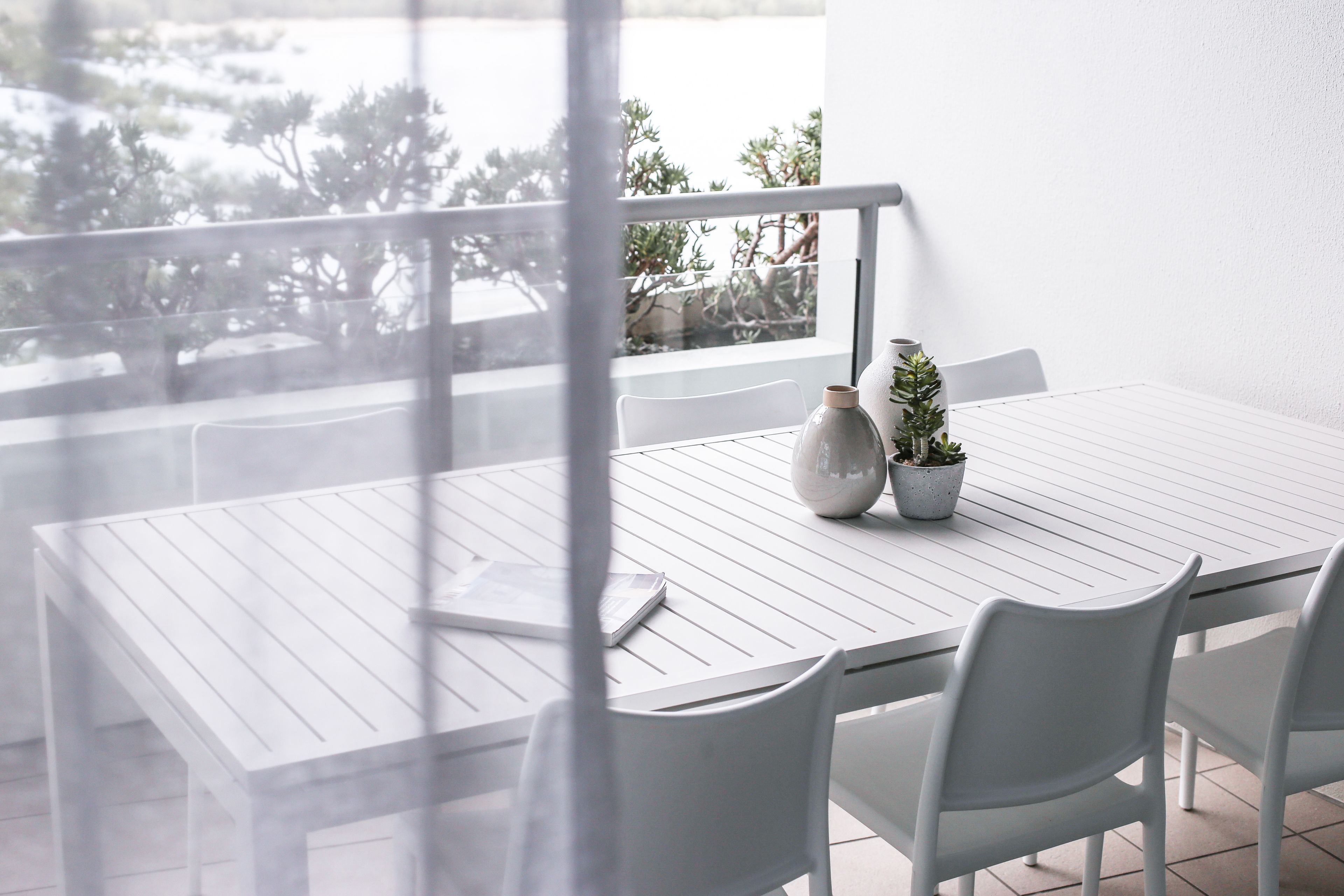 A white table with chairs and a vase on a balcony overlooking a body of water.