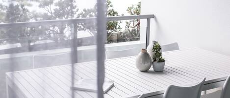 Una mesa blanca con sillas y un florero en un balcón con vista a un cuerpo de agua.