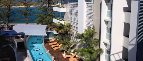 Un espace piscine aménagé dans un complexe hôtelier, avec des chaises longues et une vue sur la mer.