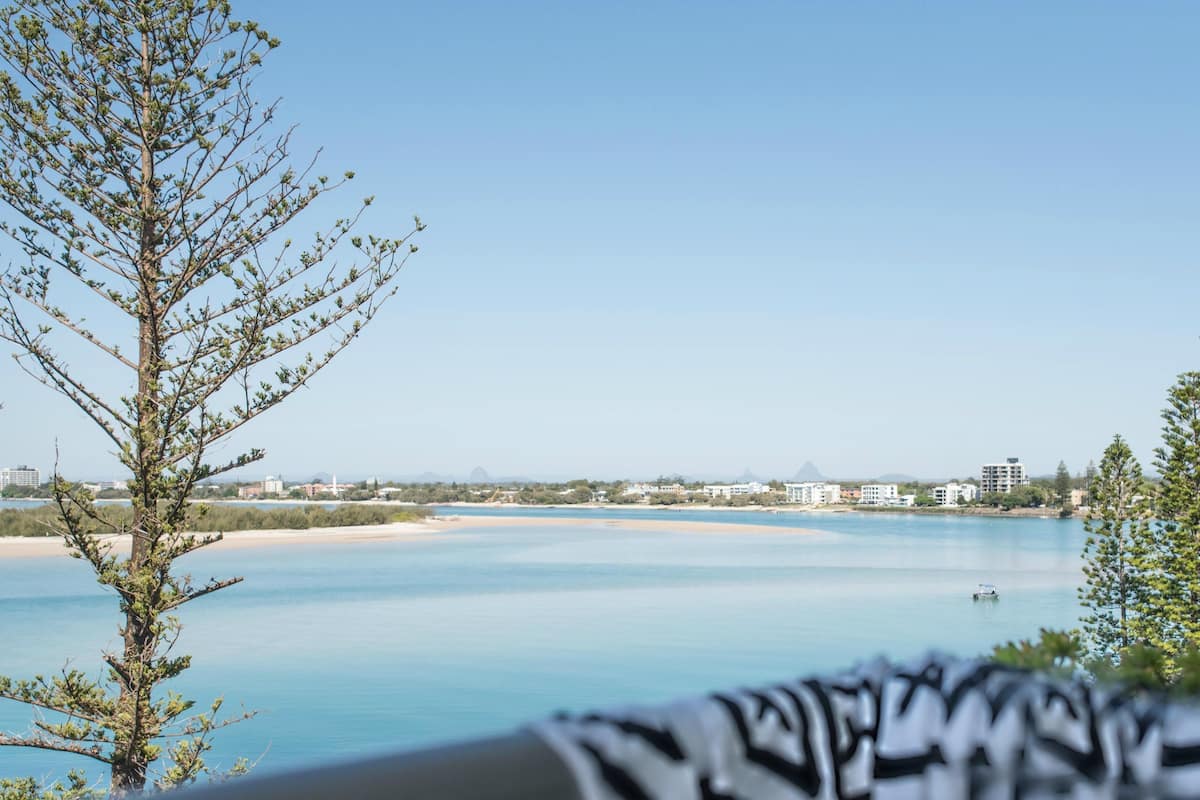 A coastal view with a clear sky, a sandy beach, and buildings in the distance.