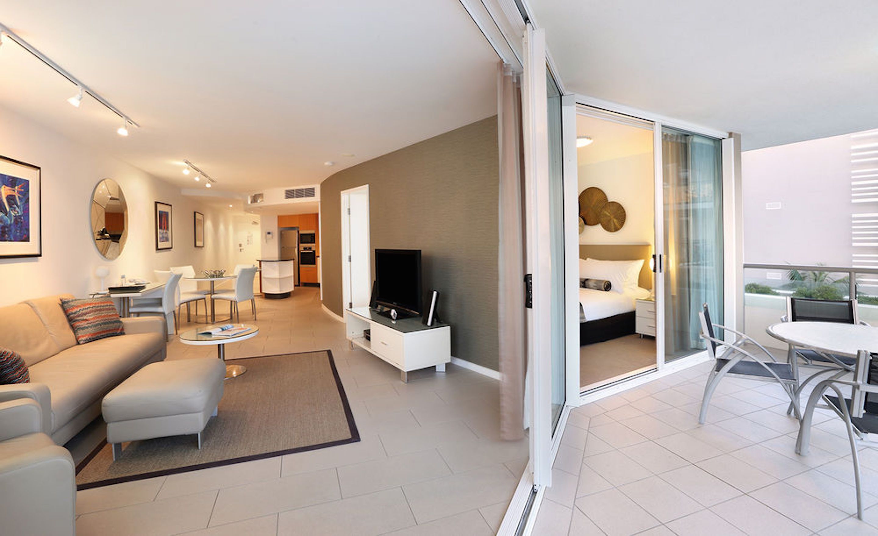 Ein modernes Wohnzimmer mit einer Couch, einem Couchtisch und einem Fernseher. Es gibt einen Balkon mit Tisch und Stühlen.