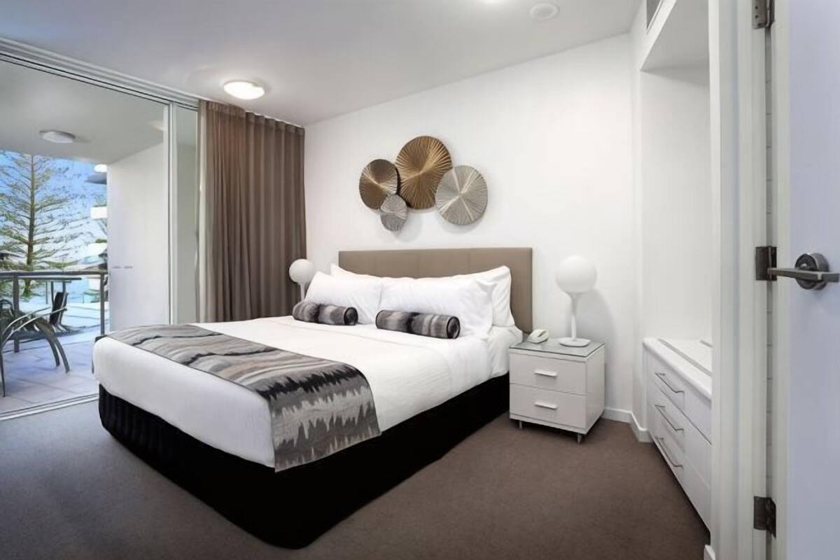 A modern hotel room with a large bed, a bedside table, a nightstand, and a view of the outdoors.