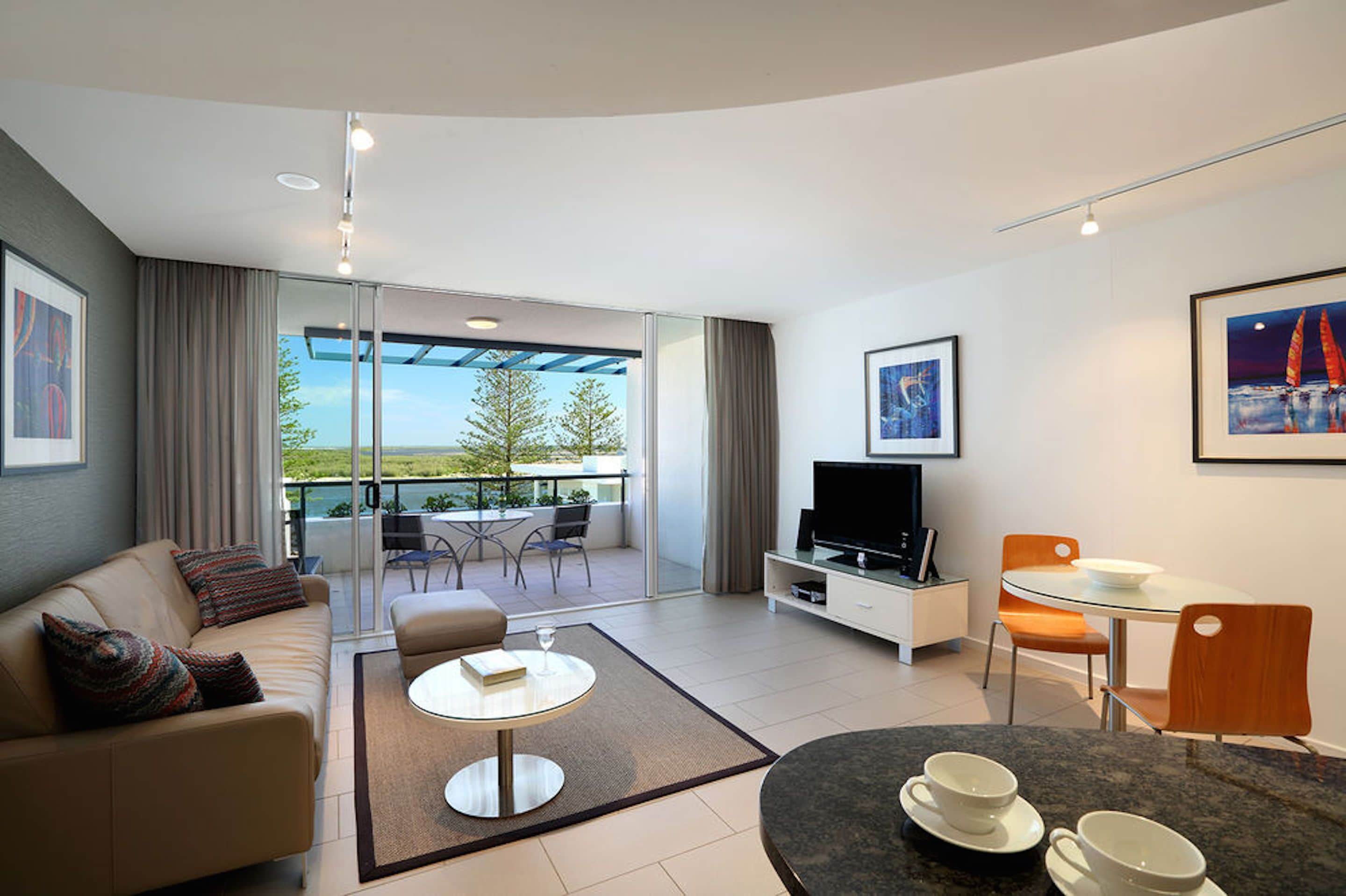 A modern living room with a sofa, coffee table, TV, and dining area.