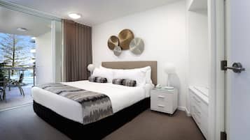 A modern hotel room with a large bed, a bedside table, a nightstand, and a view of the outdoors.