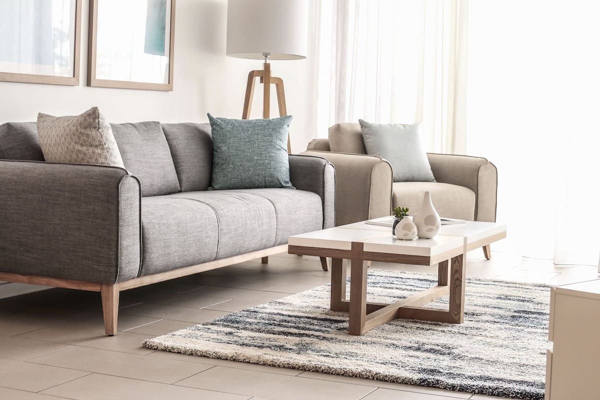 A modern living room with a grey sofa, a beige armchair, a wooden coffee table, and a striped rug.