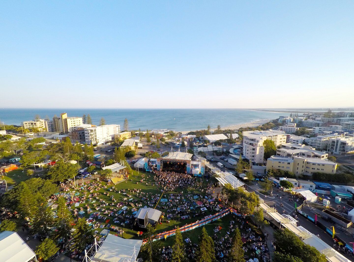 A coastal cityscape with a large open public space hosting a crowd, surrounded by residential buildings and a view of the sea.