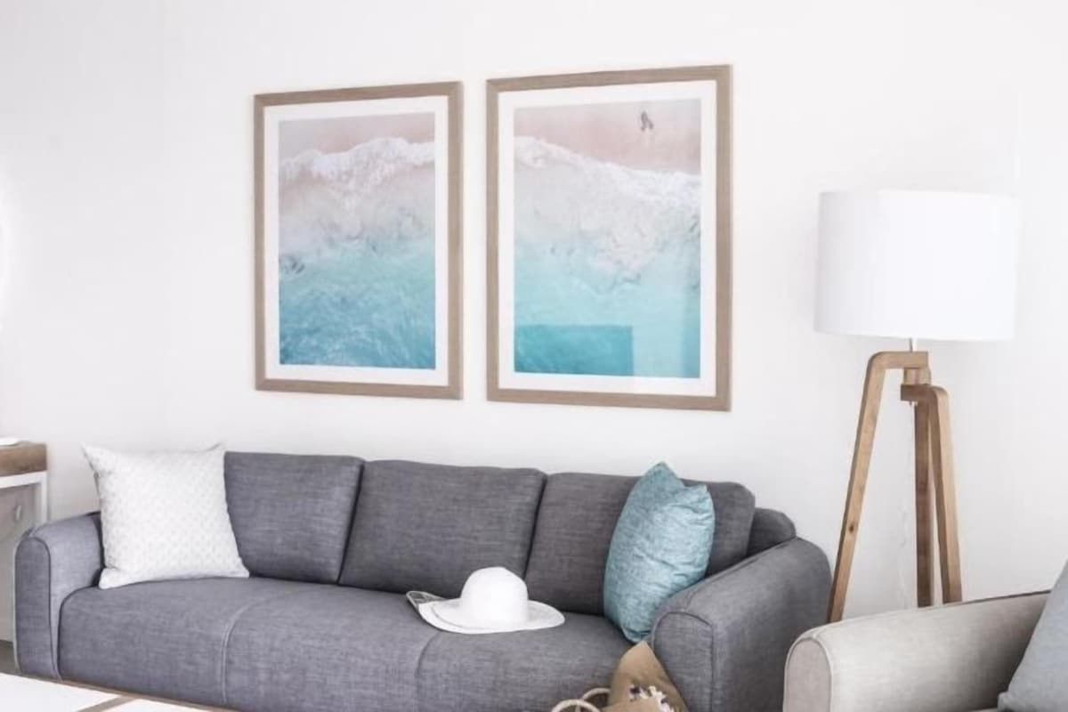 A grey sofa with a white hat and a blue pillow, a floor lamp, and two framed abstract paintings on the wall.