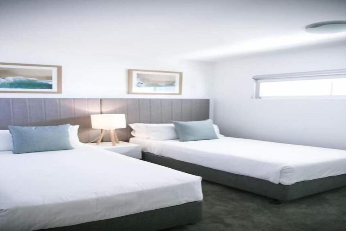 A hotel room with two beds, a grey headboard, white bedding, a nightstand with a lamp, and framed pictures on the wall.
