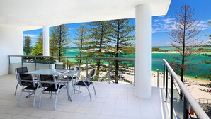 Un balcon avec une table et des chaises, donnant sur une plage et des arbres.