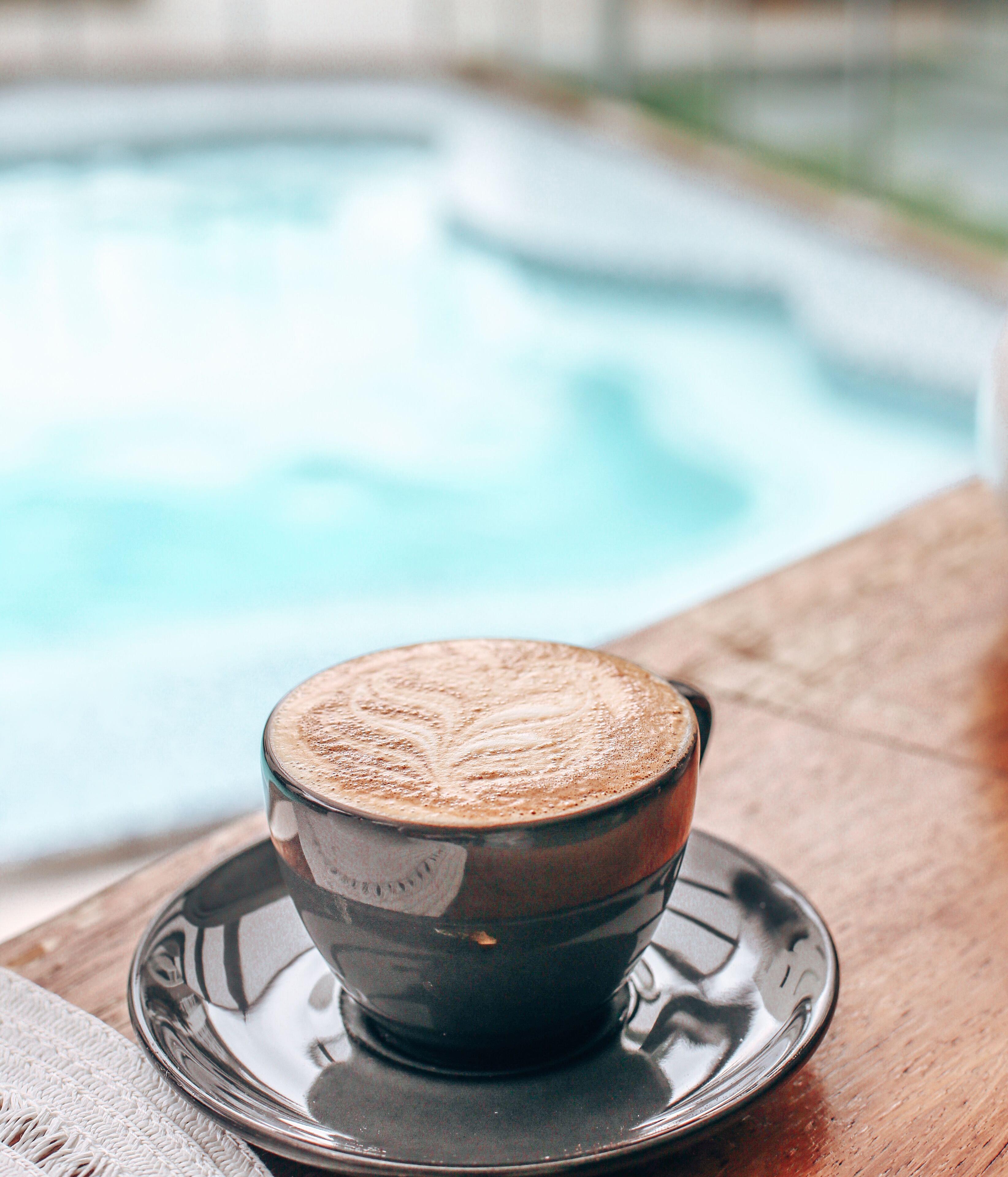 Une tasse de café posée sur une soucoupe, près d’une piscine.