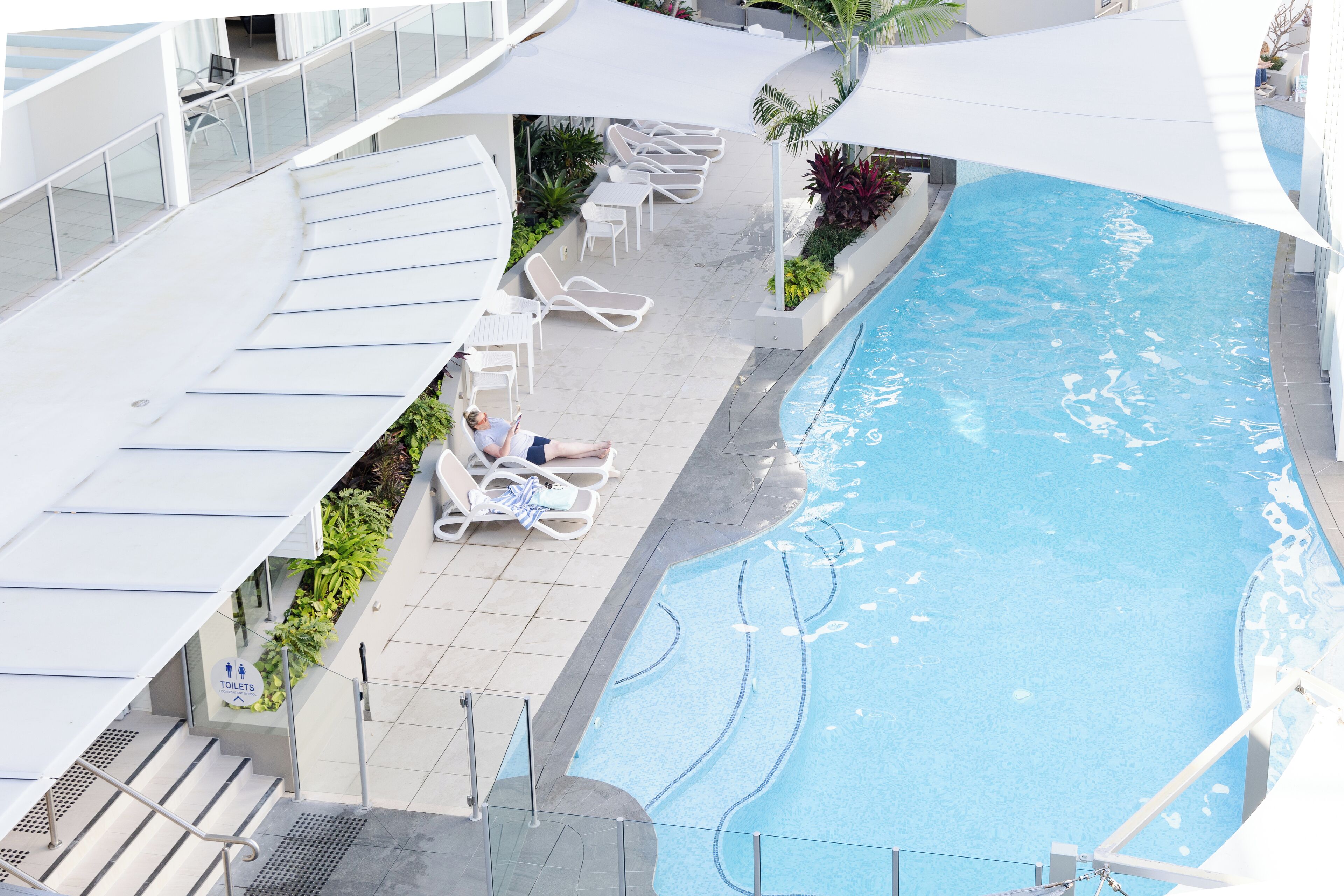 A pool area with lounge chairs and a sign indicating toilets.