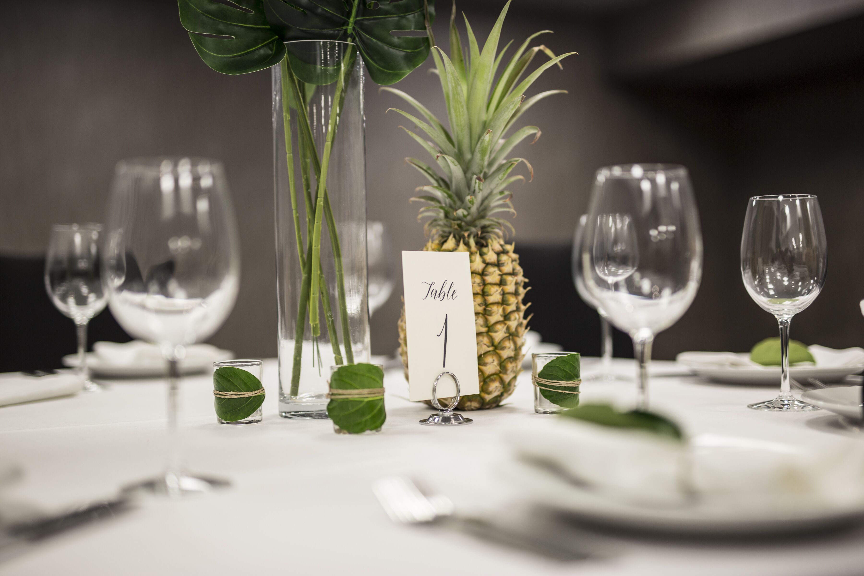 Een gedekte tafel met wijnglazen, een ananas als middelpunt en een menukaart.