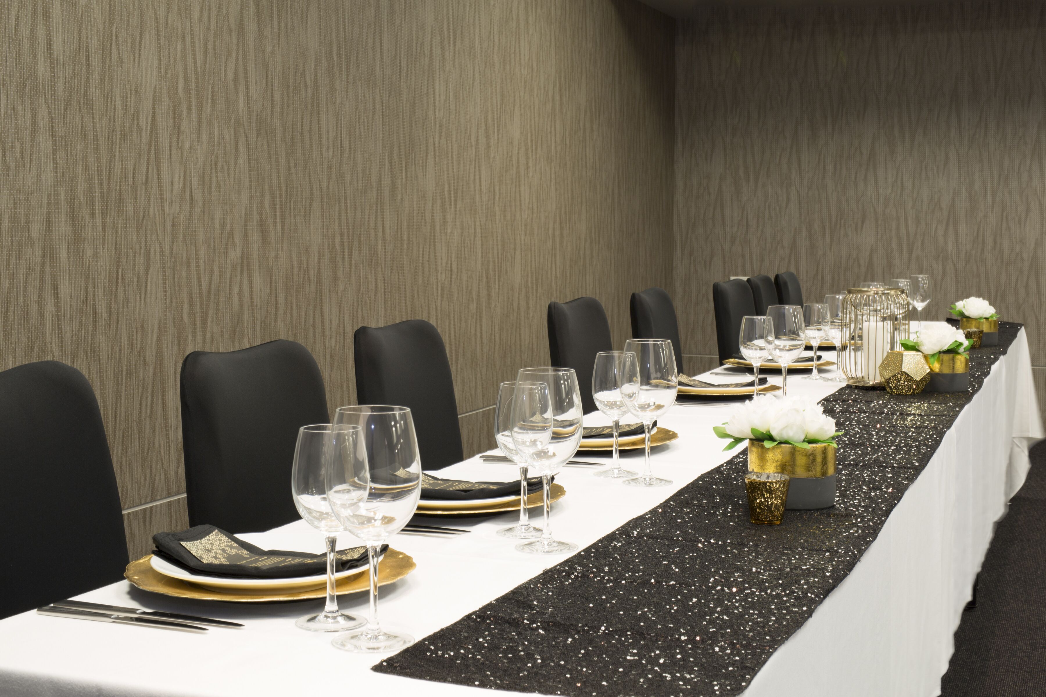 A long conference table set for a formal event with chairs, glassware, and decorative elements.