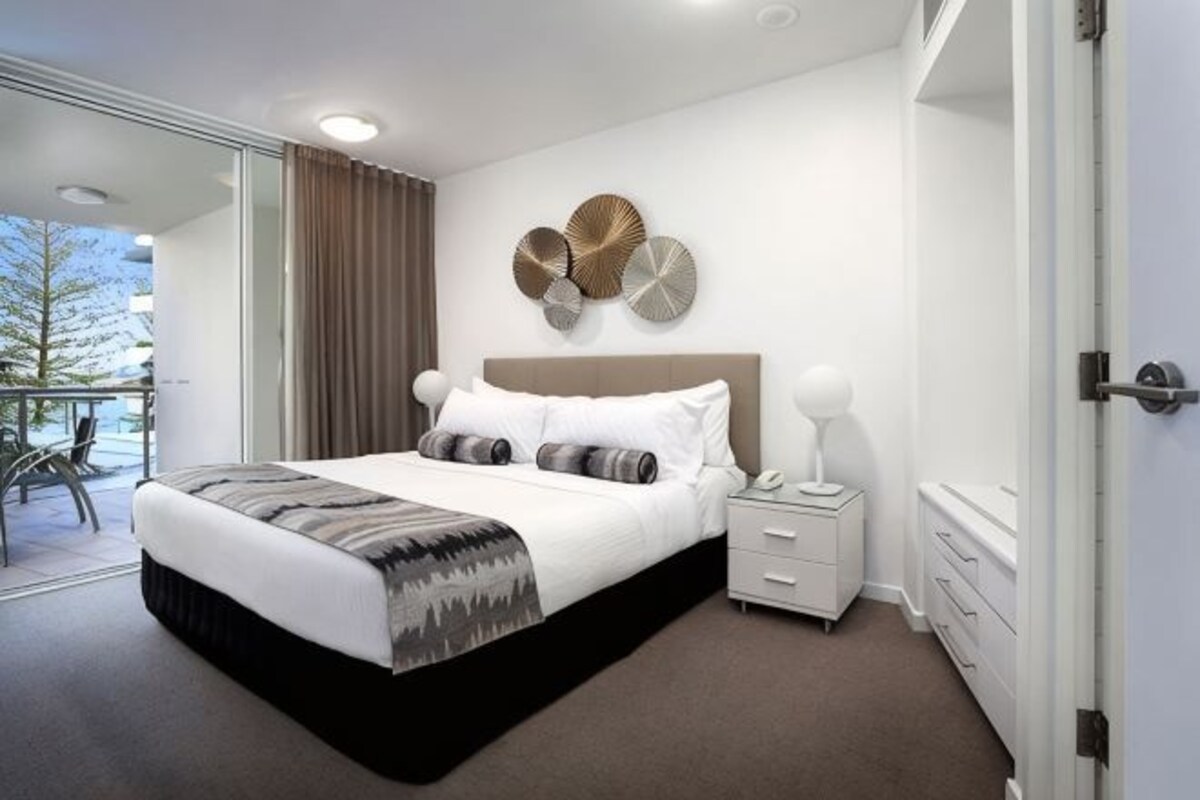 A modern hotel room with a large bed, a bedside table, a nightstand, and a view of the outdoors.