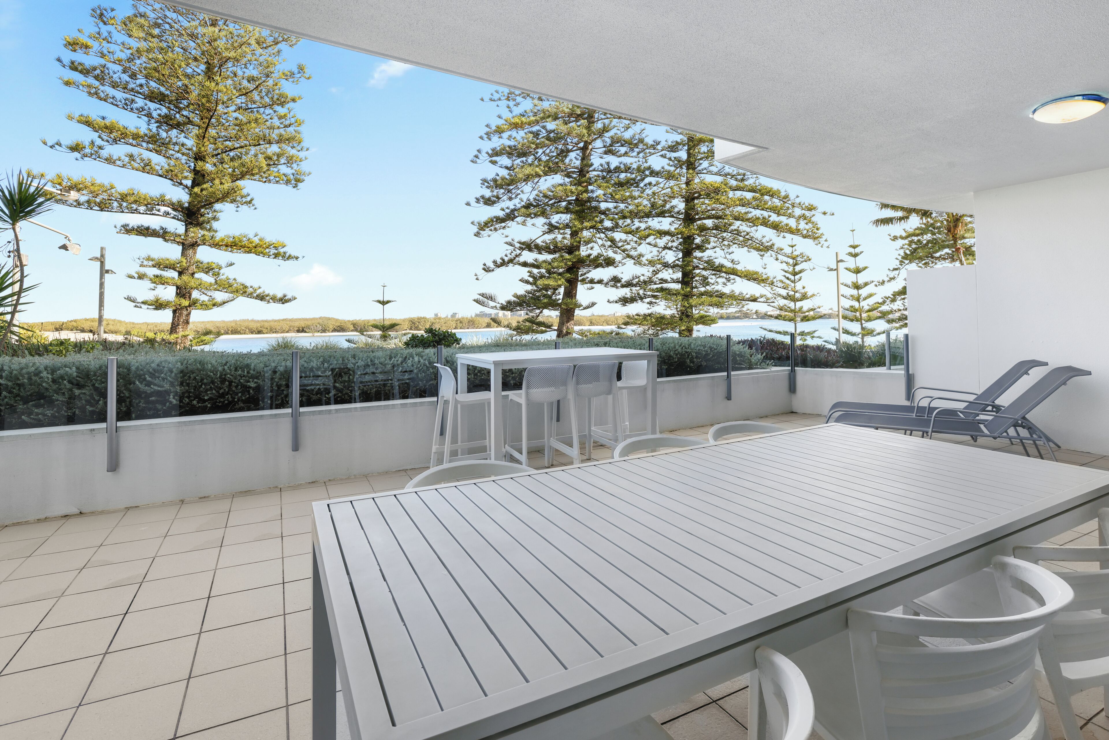 A modern outdoor patio with a table and chairs, overlooking a scenic landscape with trees and a body of water.