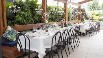A long dining table set with white tablecloths, black chairs, and various glassware and dishes.