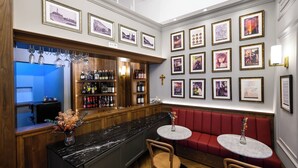 Un área de bar con una barra de madera, estantes llenos de botellas, cuadros en la pared y un asiento con mesa color rojo.
