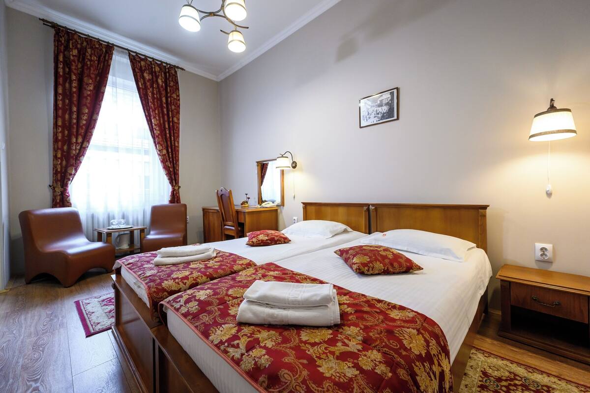 Ein Hotelzimmer mit einem großen Bett, zwei Nachttischen, einem Holznachtkästchen, einem Sessel, einem Schreibtisch und einem Spiegel.