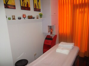 A hotel room with a bed, a desk, a chair, a shelf with decorative items, and a window with orange curtains. - Machu Picchu Suites (Lima)