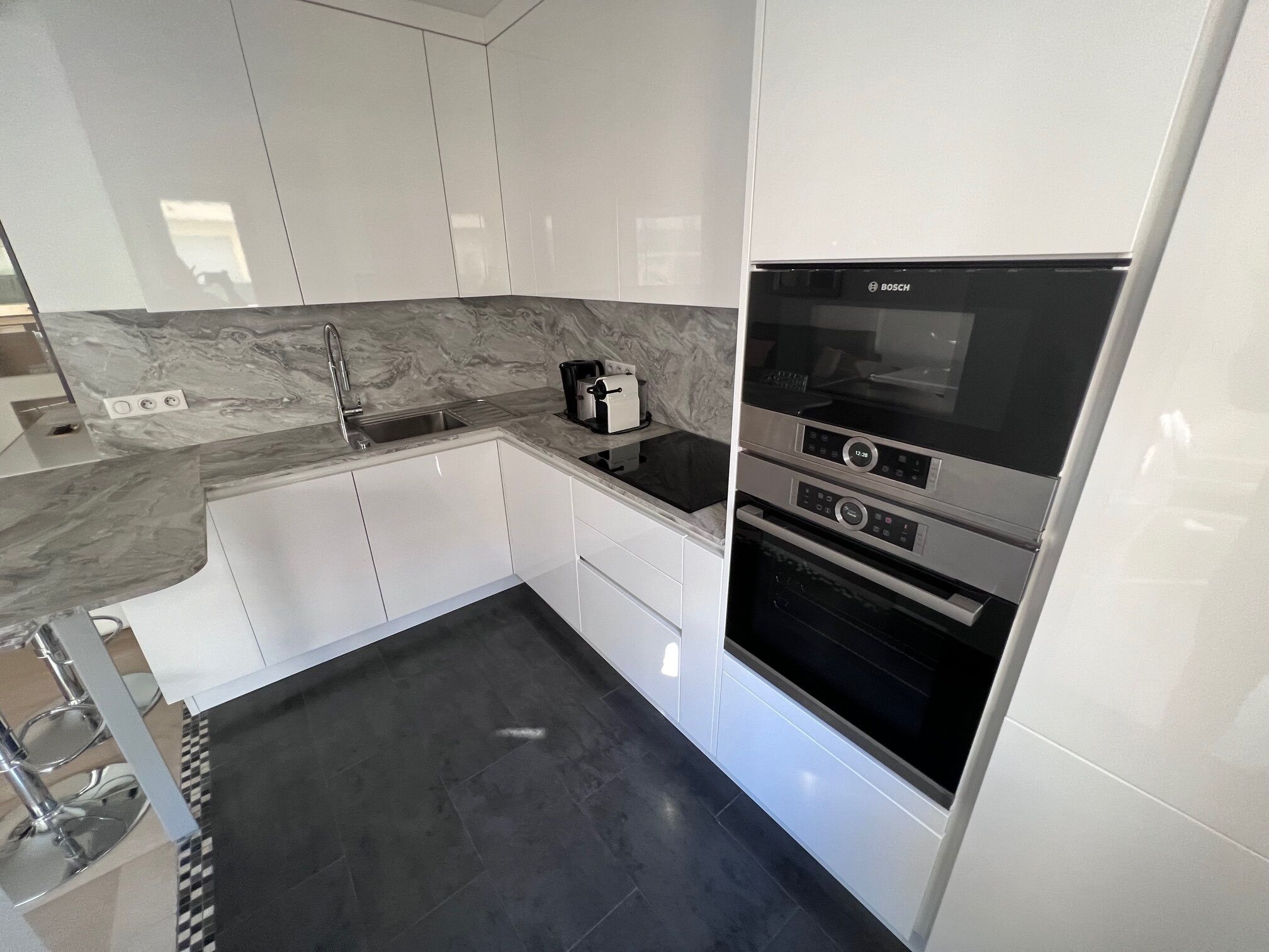 A modern kitchen with white cabinets, a marble countertop, a Bosch oven, and a black floor.