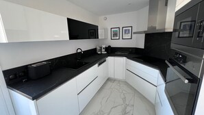 A modern kitchen with white cabinets, black countertops, a built-in oven, and a microwave. - Riviera Eden Palace (Cannes)