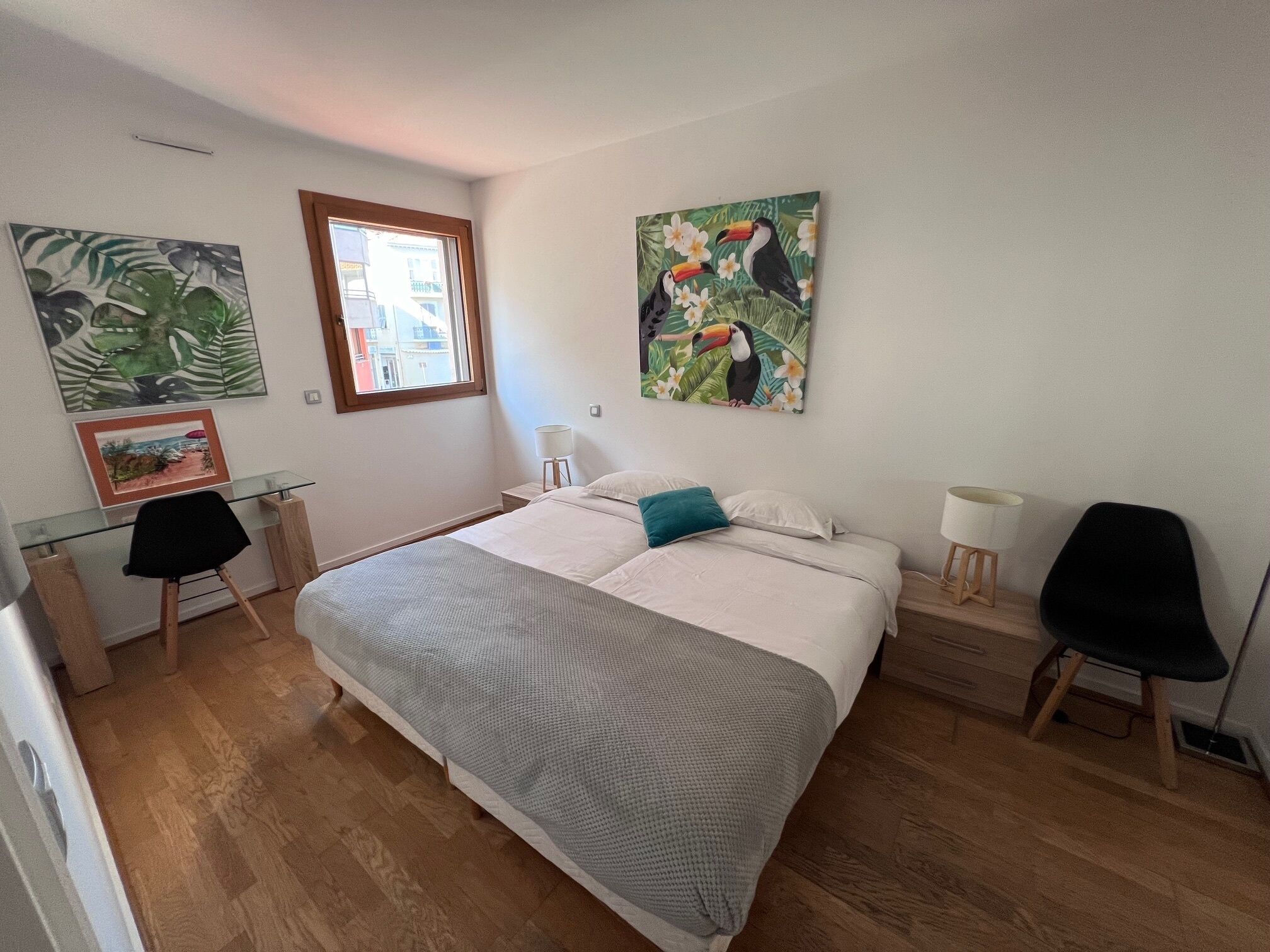 Een slaapkamer met een groot bed, een bureau met stoel, een raam en kunstwerken aan de muur.