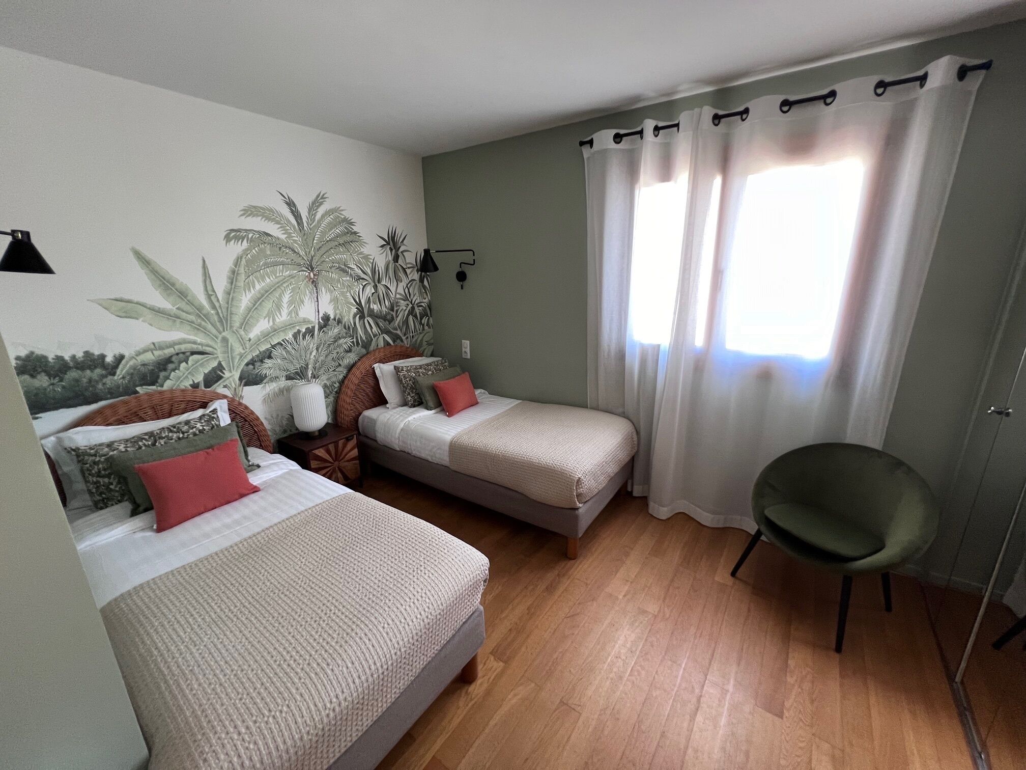 A bedroom with two beds, a chair, a wall mural, and a window with curtains.