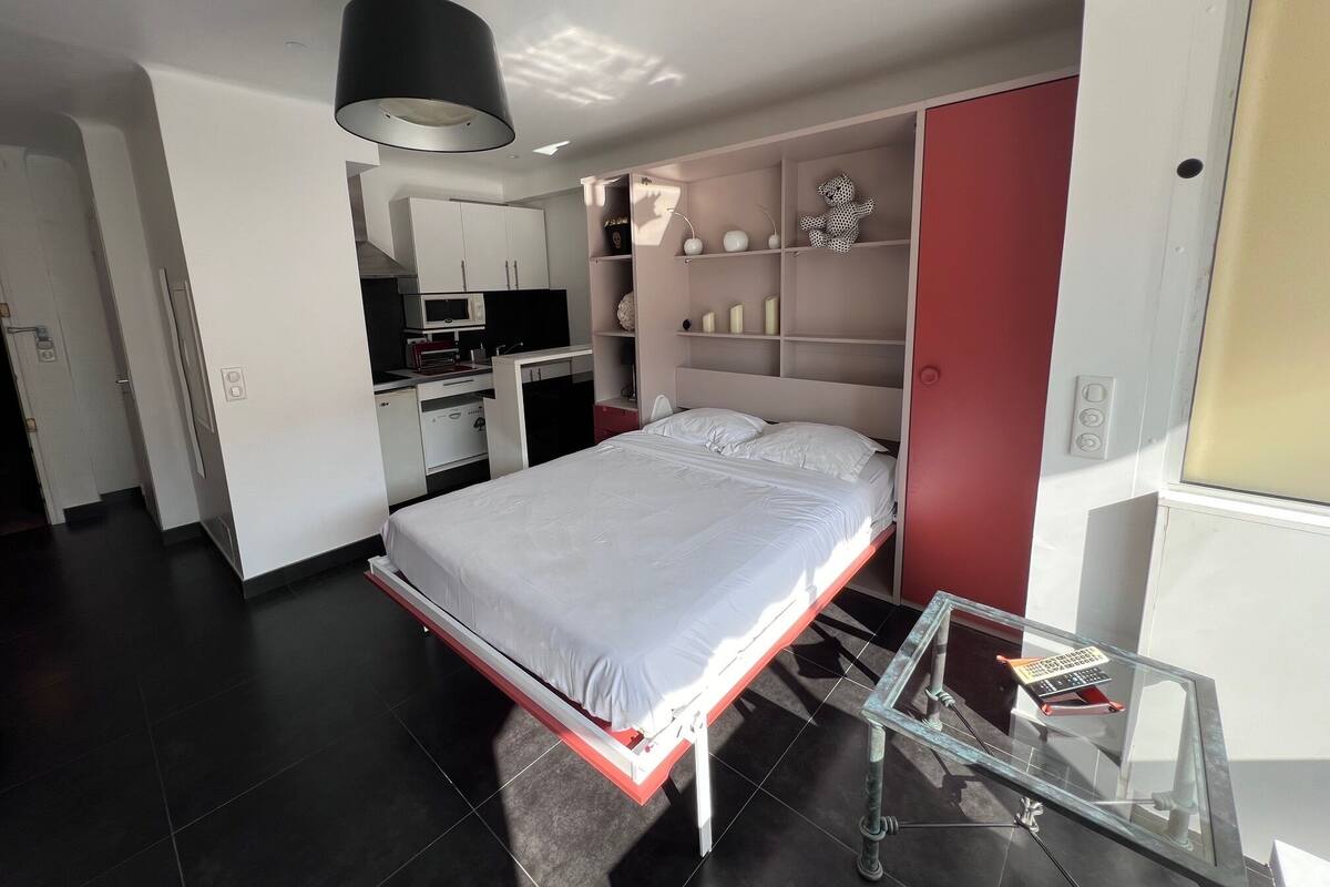 A modern bedroom with a bed, a desk, and a kitchenette.