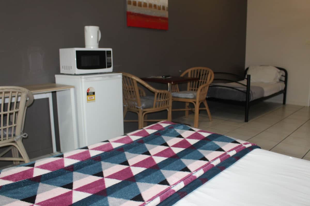A hotel room with a bed, a microwave, a small refrigerator, a wooden chair, and a table.
