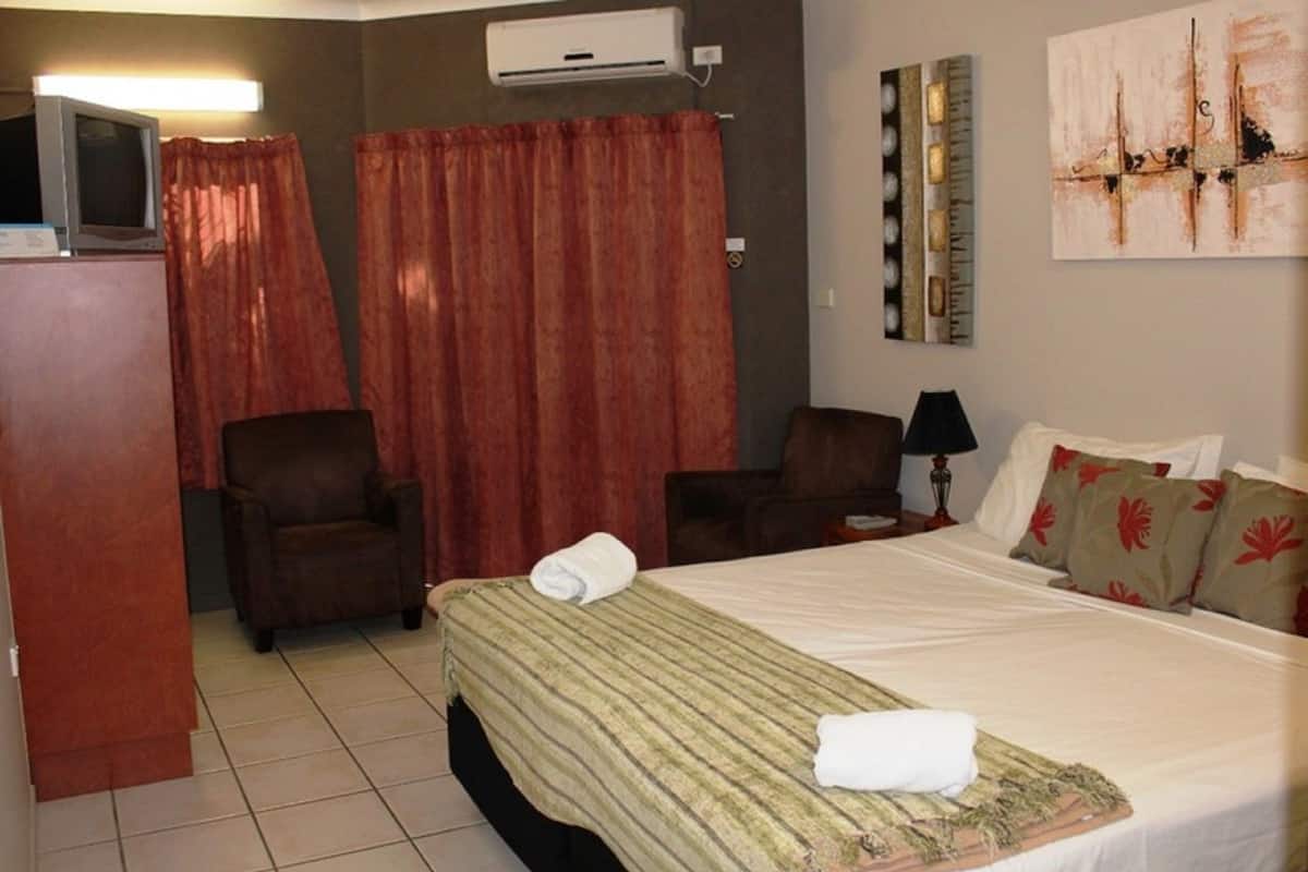 A hotel room with a bed, a chair, a desk, an air conditioner, and a painting on the wall.