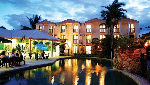 A hotel with a swimming pool, outdoor seating, and a well-lit building facade.