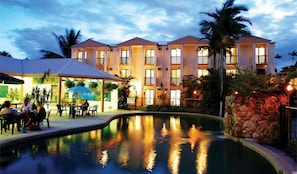 A hotel with a swimming pool, outdoor seating, and a well-lit building facade. - Bohemia Resort Cairns (Cairns North)