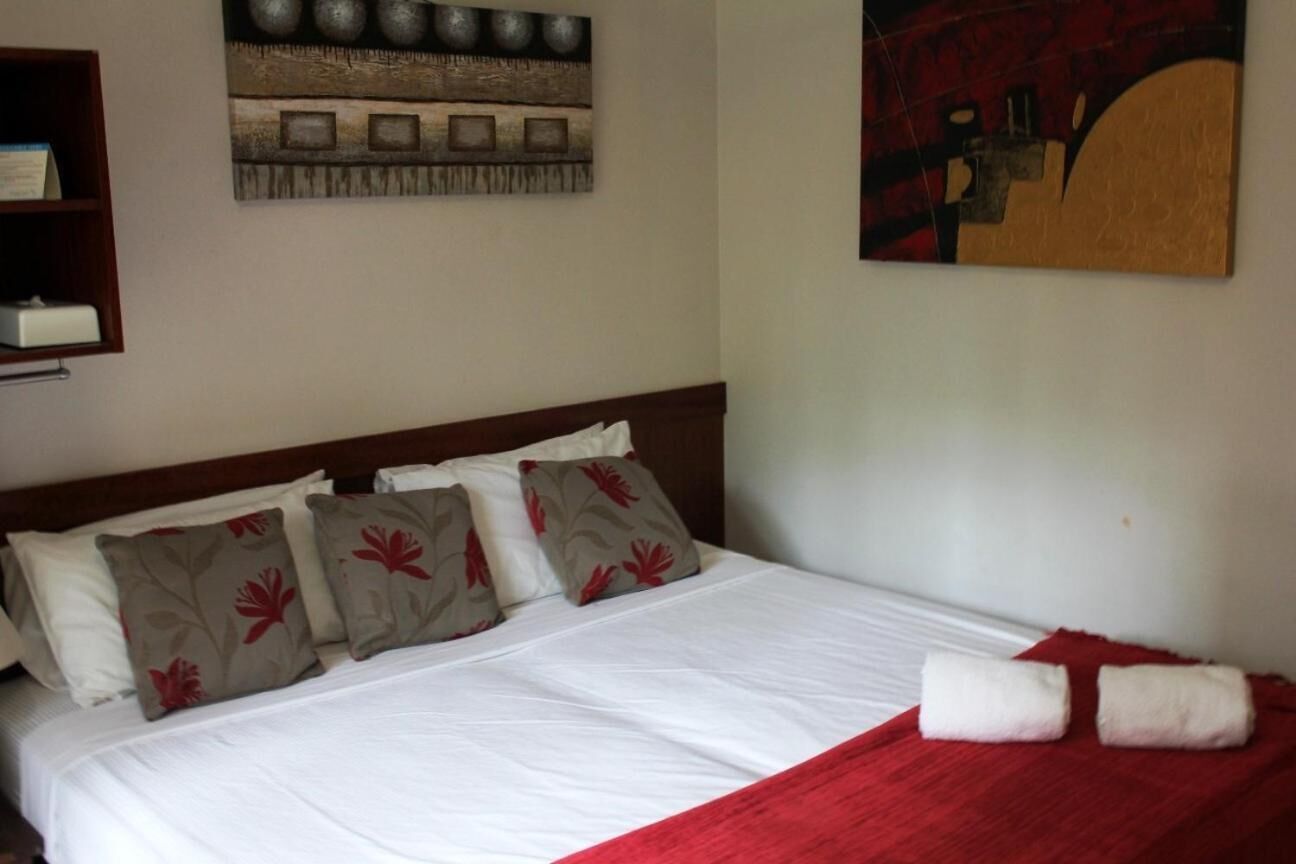 A neatly made bed with white bedding and red accents, a wooden headboard, and a red throw blanket.