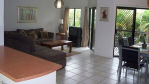 A living room with a sofa, coffee table, TV, and a dining area with chairs and a table.