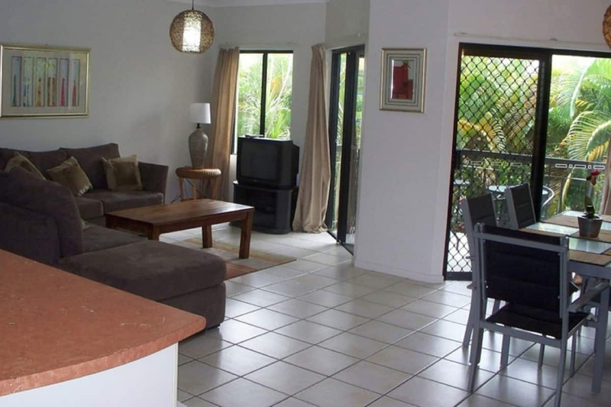 A living room with a sofa, coffee table, TV, and a dining area with chairs and a table.