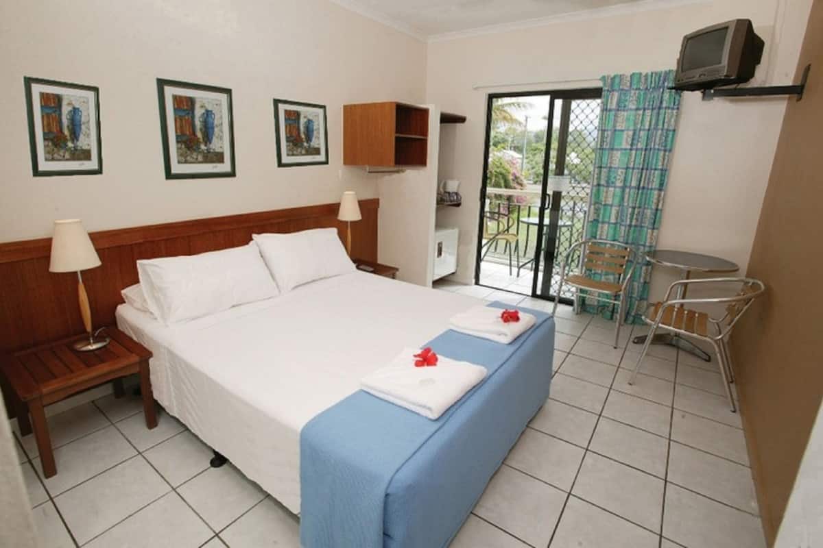 A hotel room with a bed, bedside tables, a TV, and a balcony with chairs.