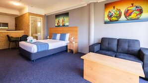 A hotel room with a bed, a desk, a couch, and artwork on the walls.