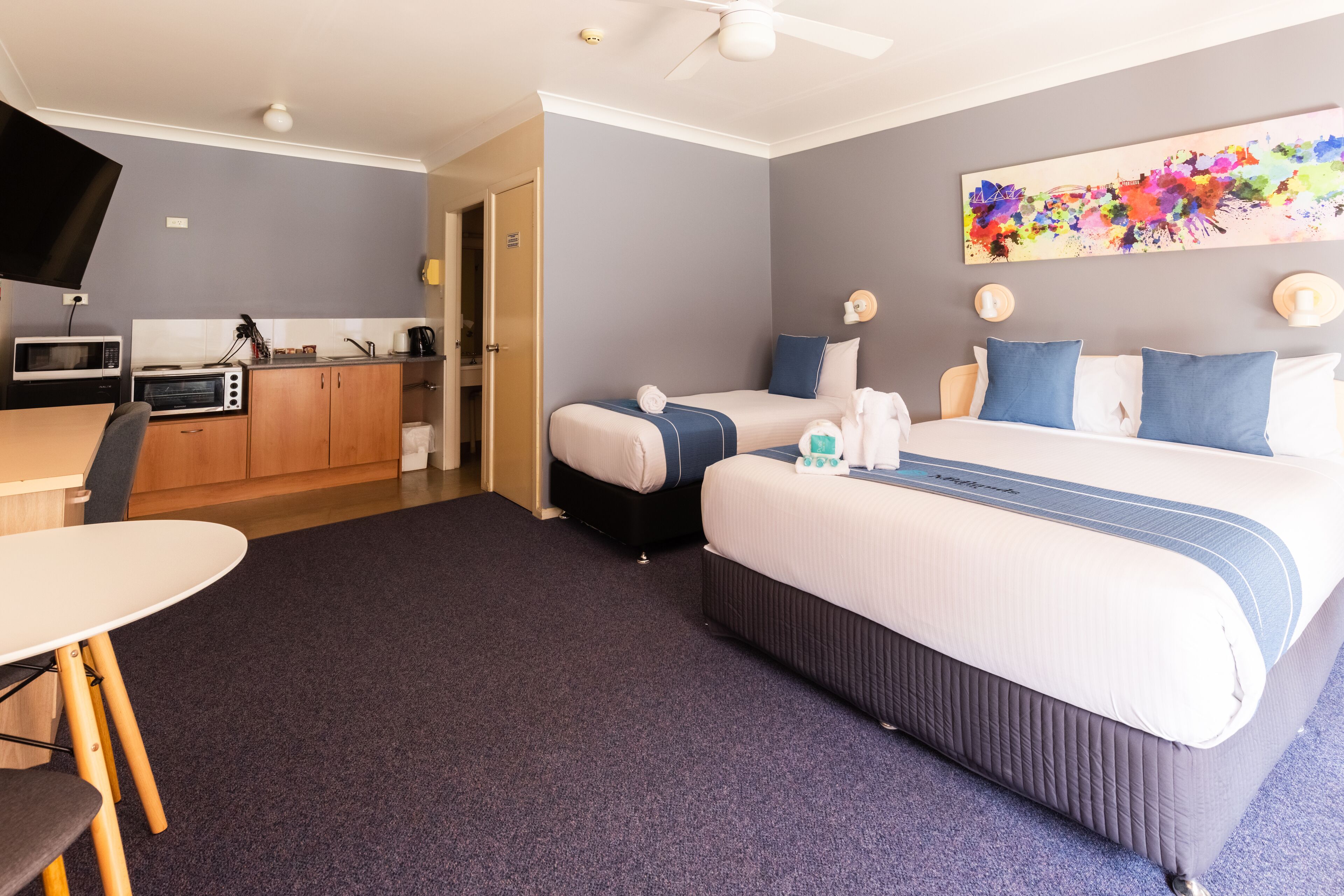 A hotel room with a bed, bedside tables, a desk with a chair, a microwave, and a television.