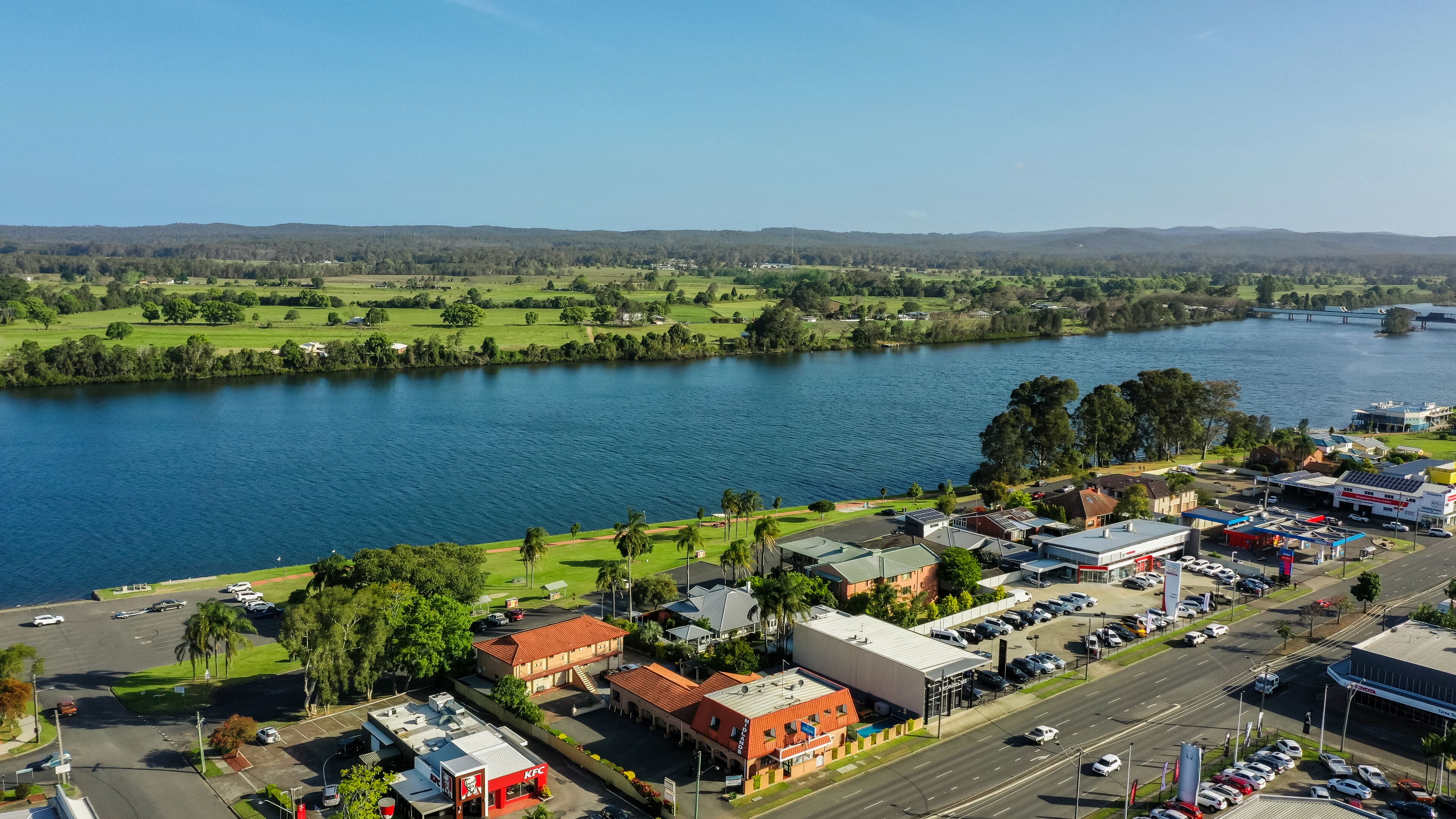 A KFC restaurant with a parking lot and a view of a river and green fields.