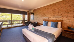 A hotel room with a large bed, a brick wall, a balcony with chairs, and a desk with a chair.