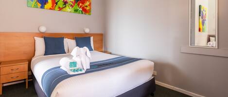 Una cama bien hecha con colcha azul y blanca a rayas, cabecero de madera y un colorido cuadro floral en la pared superior.