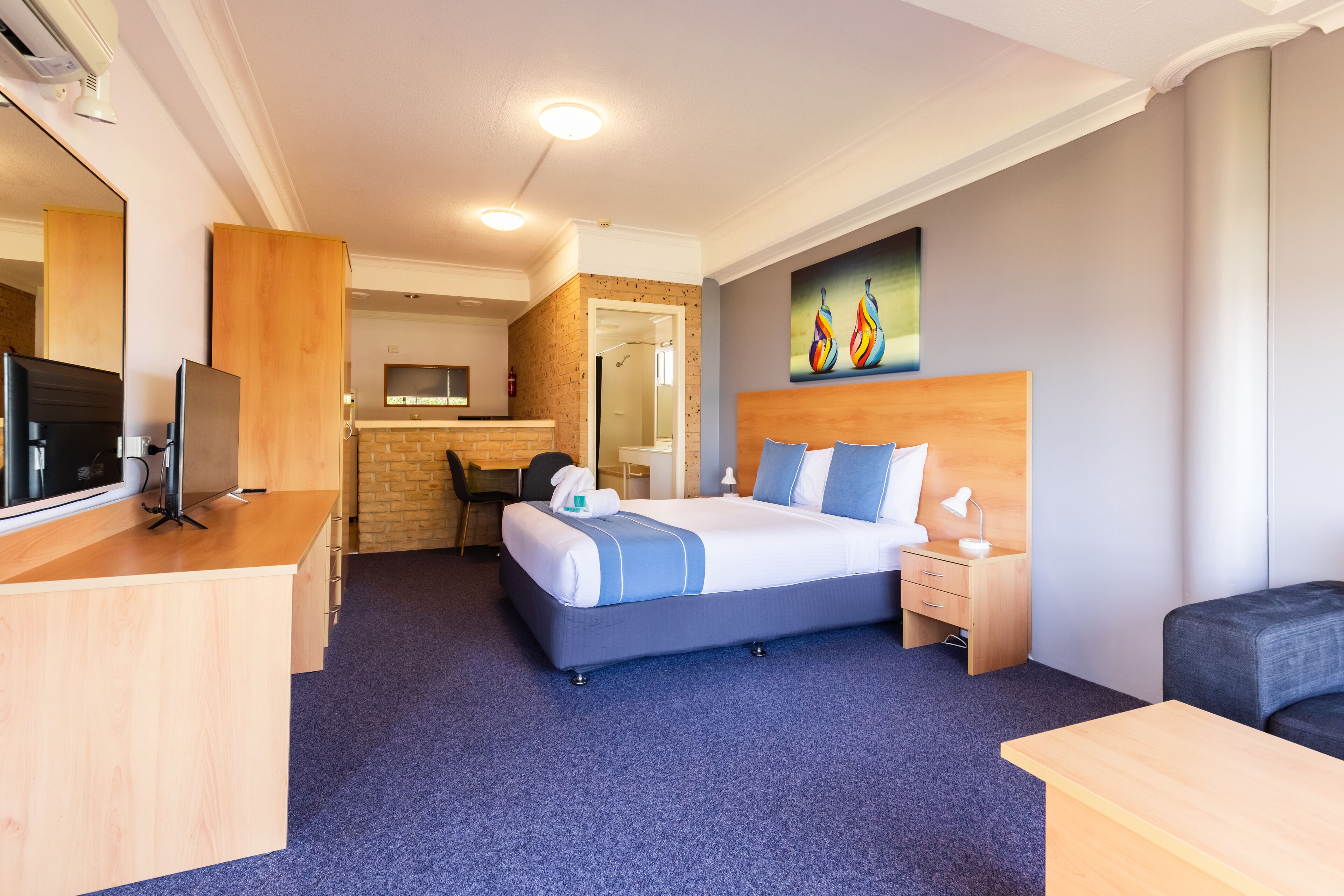 A hotel room with a bed, bedside table, desk, and a television.