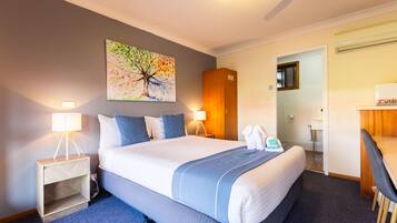 Una habitación de hotel con una cama grande, un escritorio, una silla, una mesita de noche, una lámpara y un cuadro en la pared.