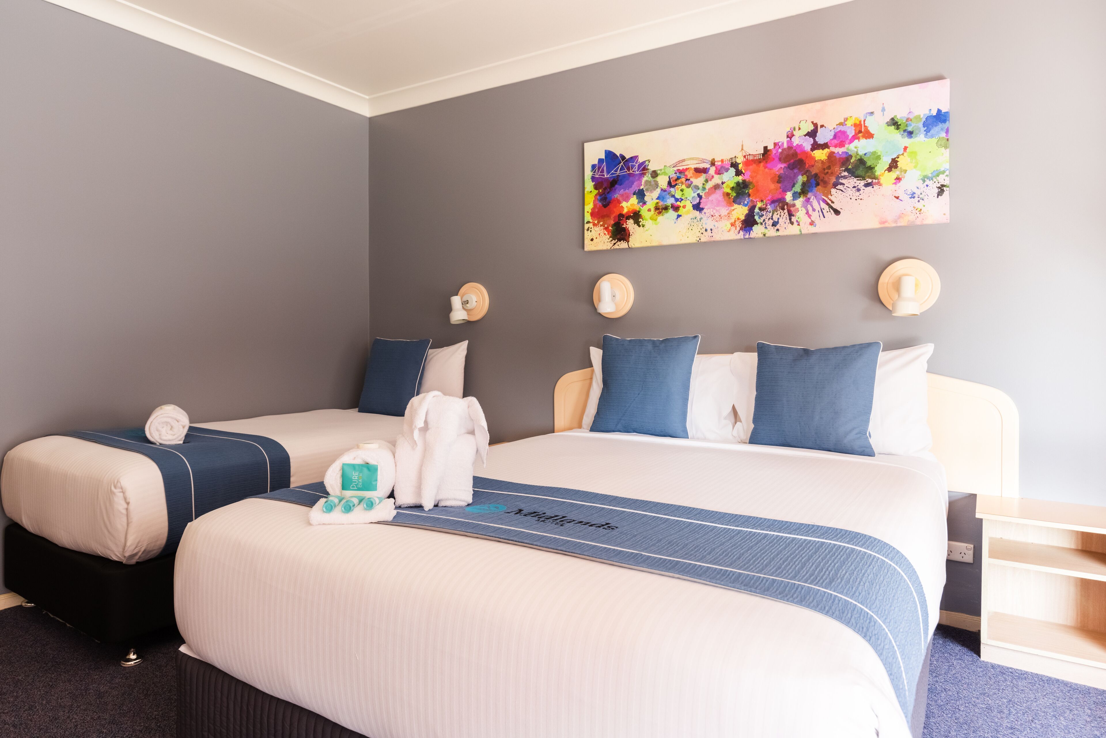 A hotel room with two beds, a large artwork on the wall, and a blue-striped bed runner.