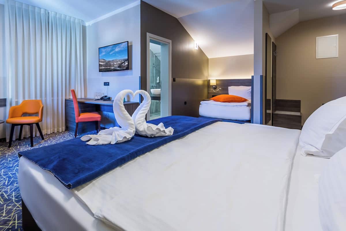 A hotel room with a large bed, a desk, a chair, and a TV on the wall.