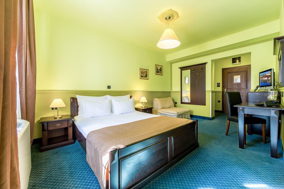 A hotel room with a bed, bedside tables, a desk, a chair, and a television.